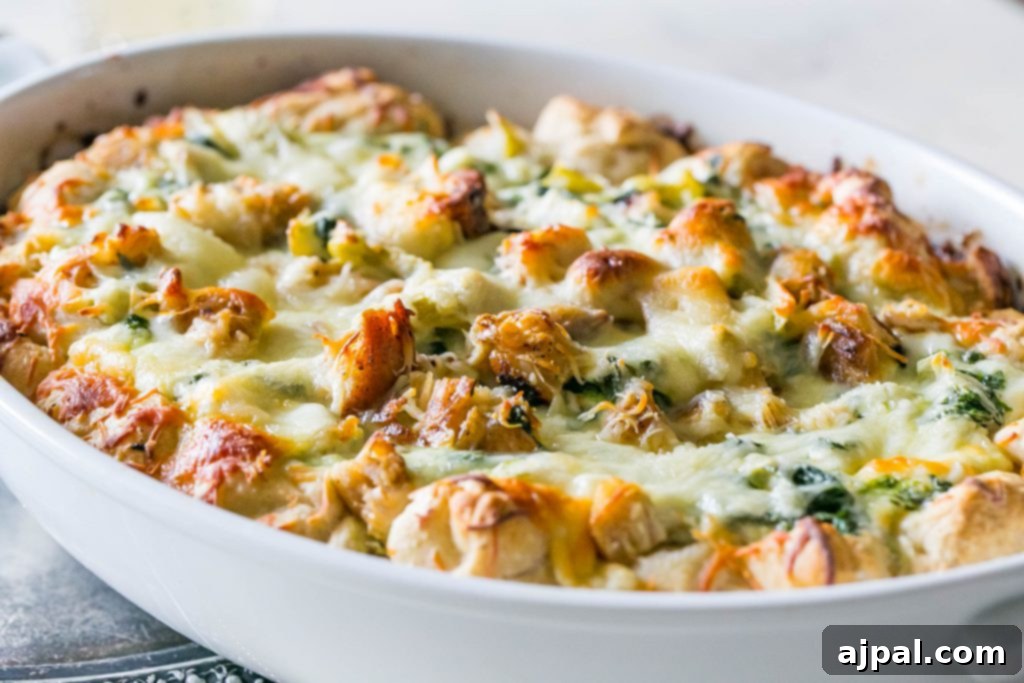 A top-down picture of the cheesy chicken, spinach, and artichoke bread dip in a white casserole dish, freshly baked and bubbling.