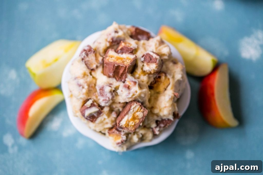 Snickers fruit dip in a bowl, with a spoon taking a scoop, showcasing its thick and creamy texture.