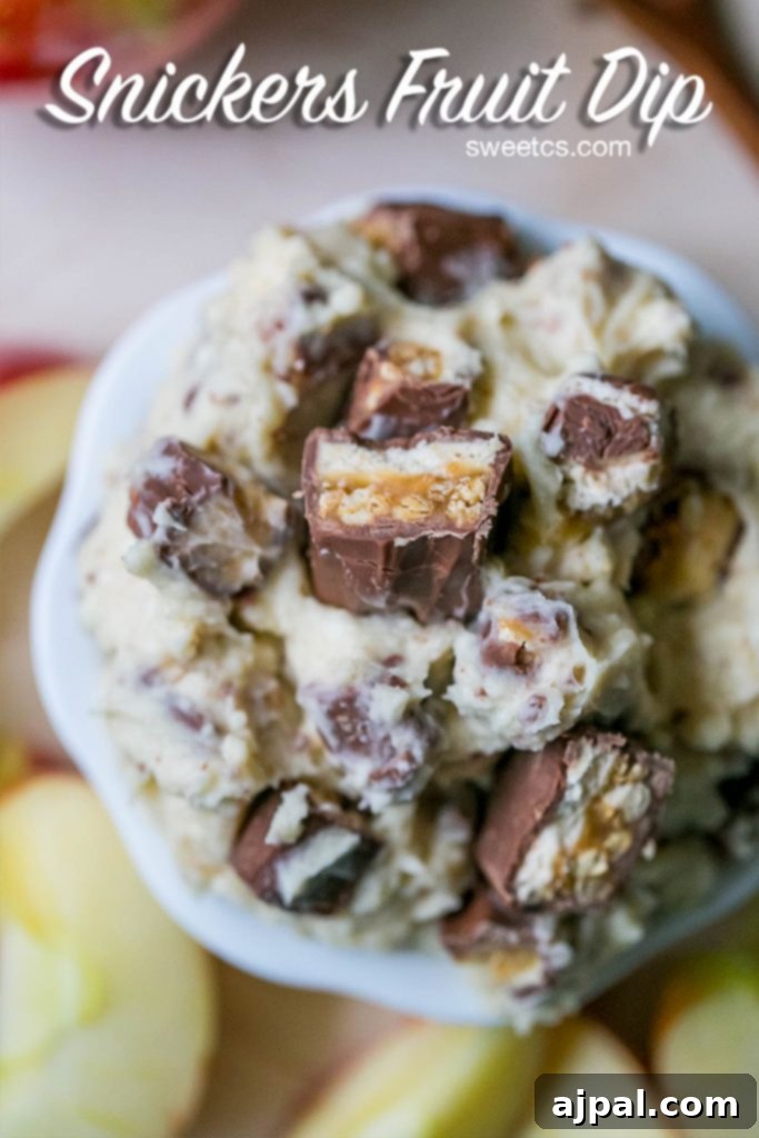 A bowl of Snickers fruit dip surrounded by a variety of fruit dippers like apples and strawberries.