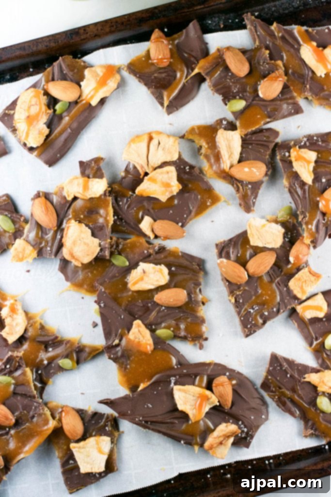 Decadent Caramel Apple Chocolate Bark 2 Rich caramel apple chocolate bark pieces on parchment paper, adorned with nuts and caramel drizzle.