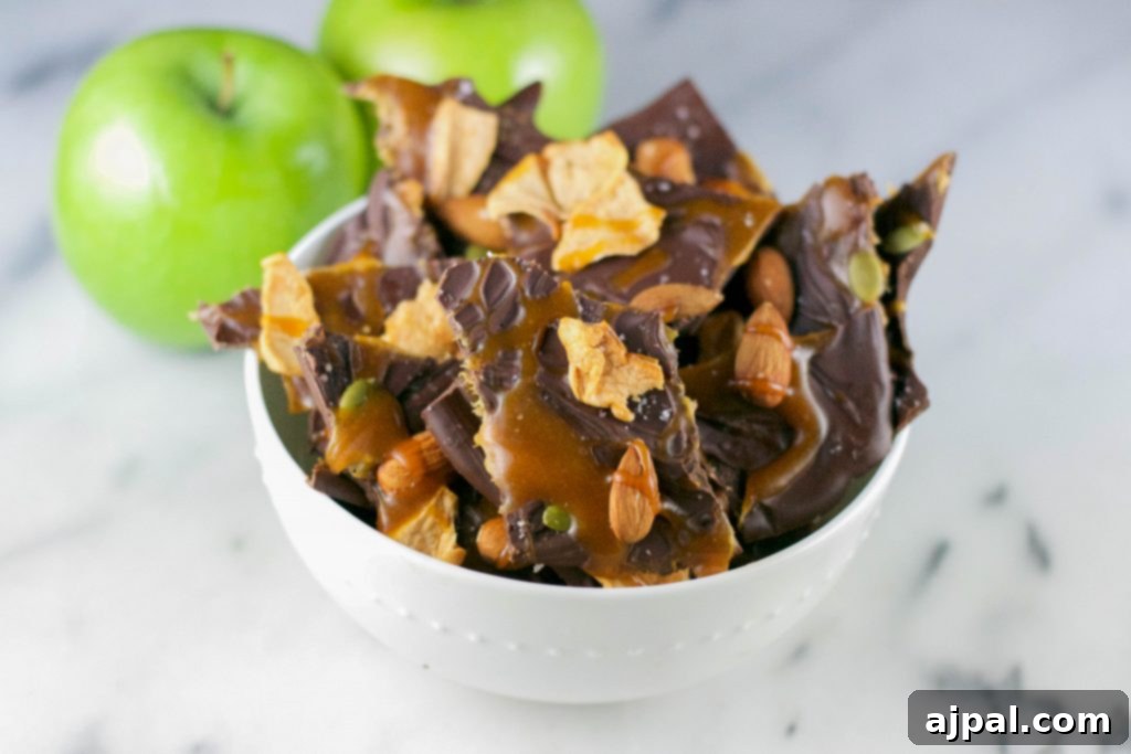 Decadent Caramel Apple Chocolate Bark 3 A bowl filled with broken pieces of caramel apple chocolate bark, featuring nuts and caramel swirls.