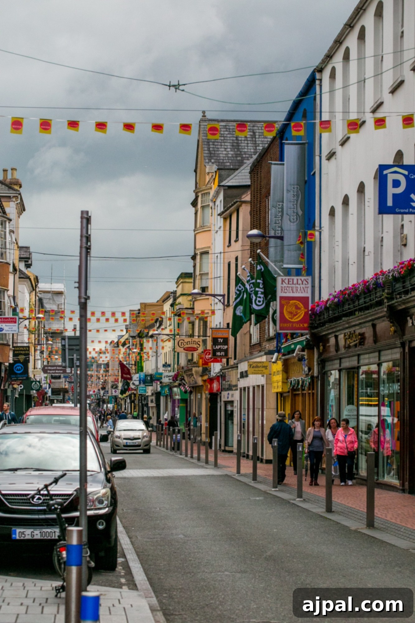 Colorful buildings and shops line a quaint street in Cork, Ireland, under a blue sky.