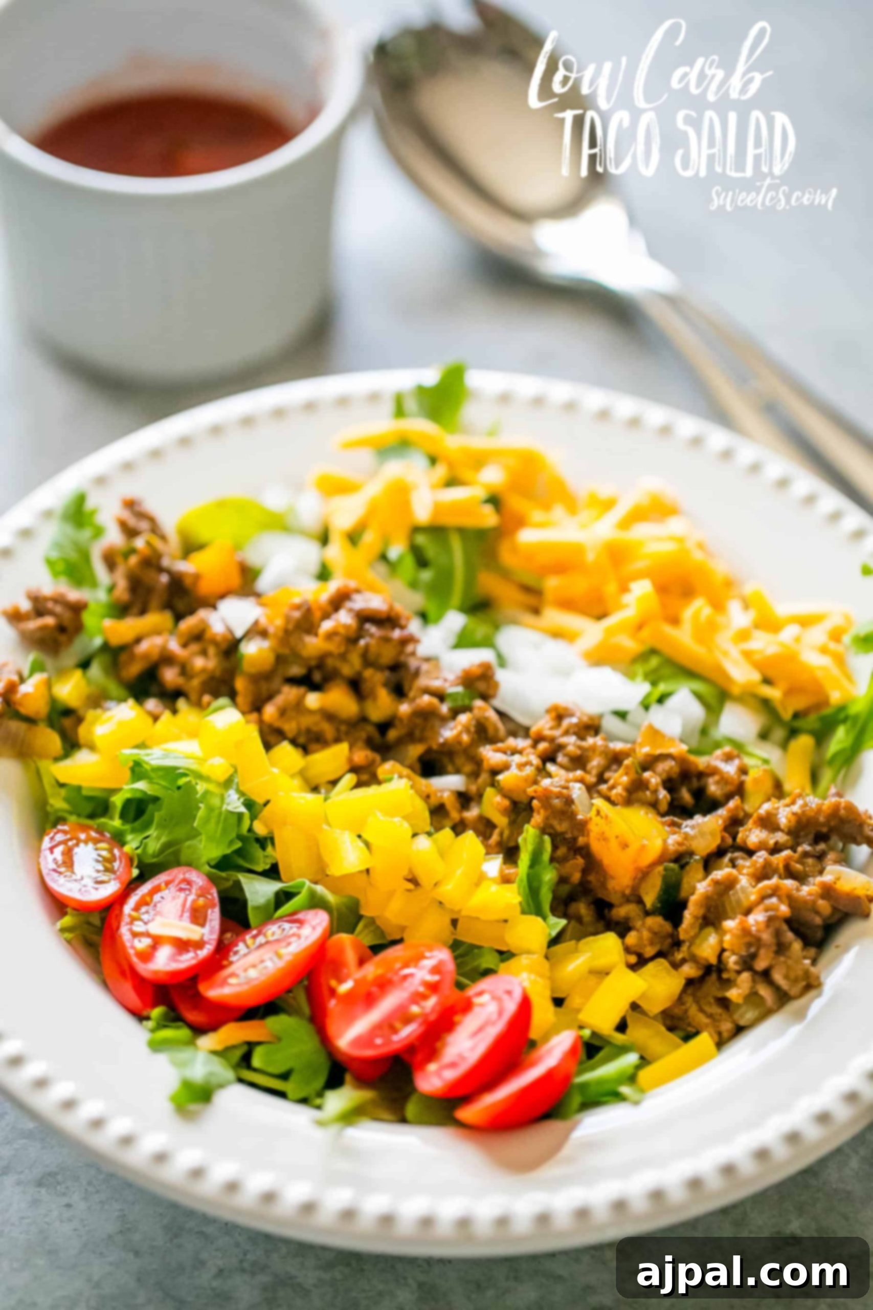 A vibrant low carb taco salad with seasoned ground beef, bell peppers, onions, tomatoes, cheese, and fresh lettuce on a white plate.