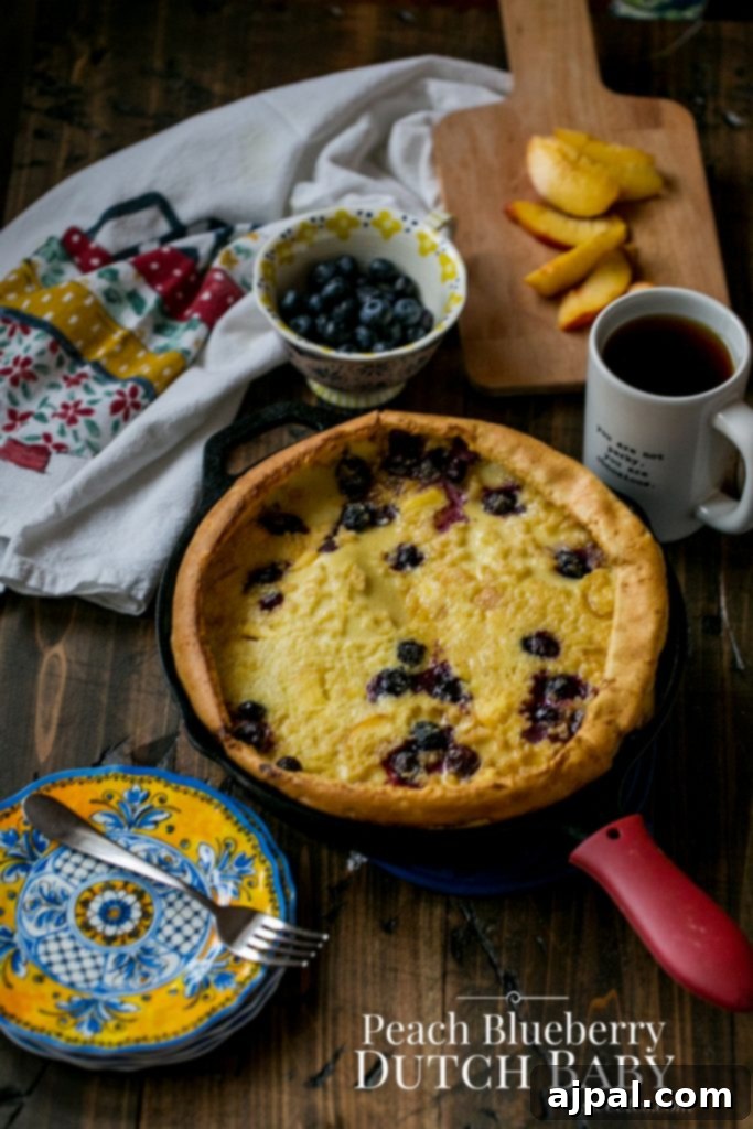 Golden puffy Dutch baby pancake with fresh peaches and blueberries in a cast iron skillet