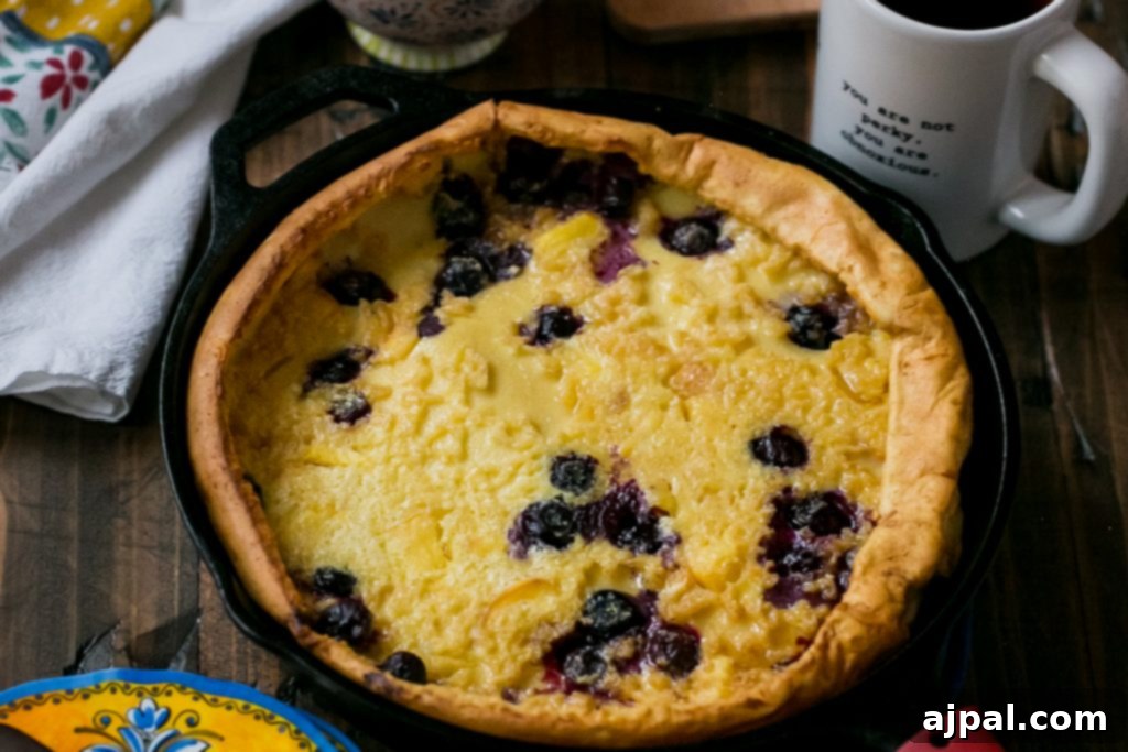 Ingredients for Dutch baby pancake laid out, including eggs, milk, flour, butter, peaches, and blueberries