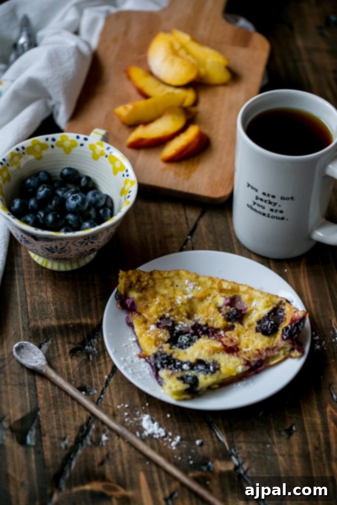 Freshly baked Dutch baby pancake with peaches and blueberries, dusted with powdered sugar