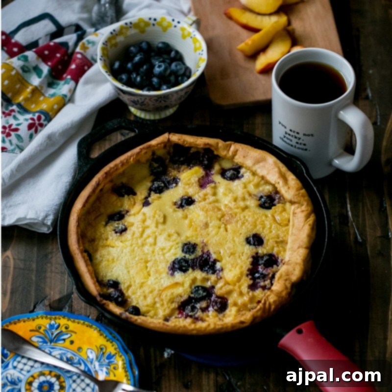A serving of Dutch baby pancake with peaches, blueberries, and powdered sugar on a plate