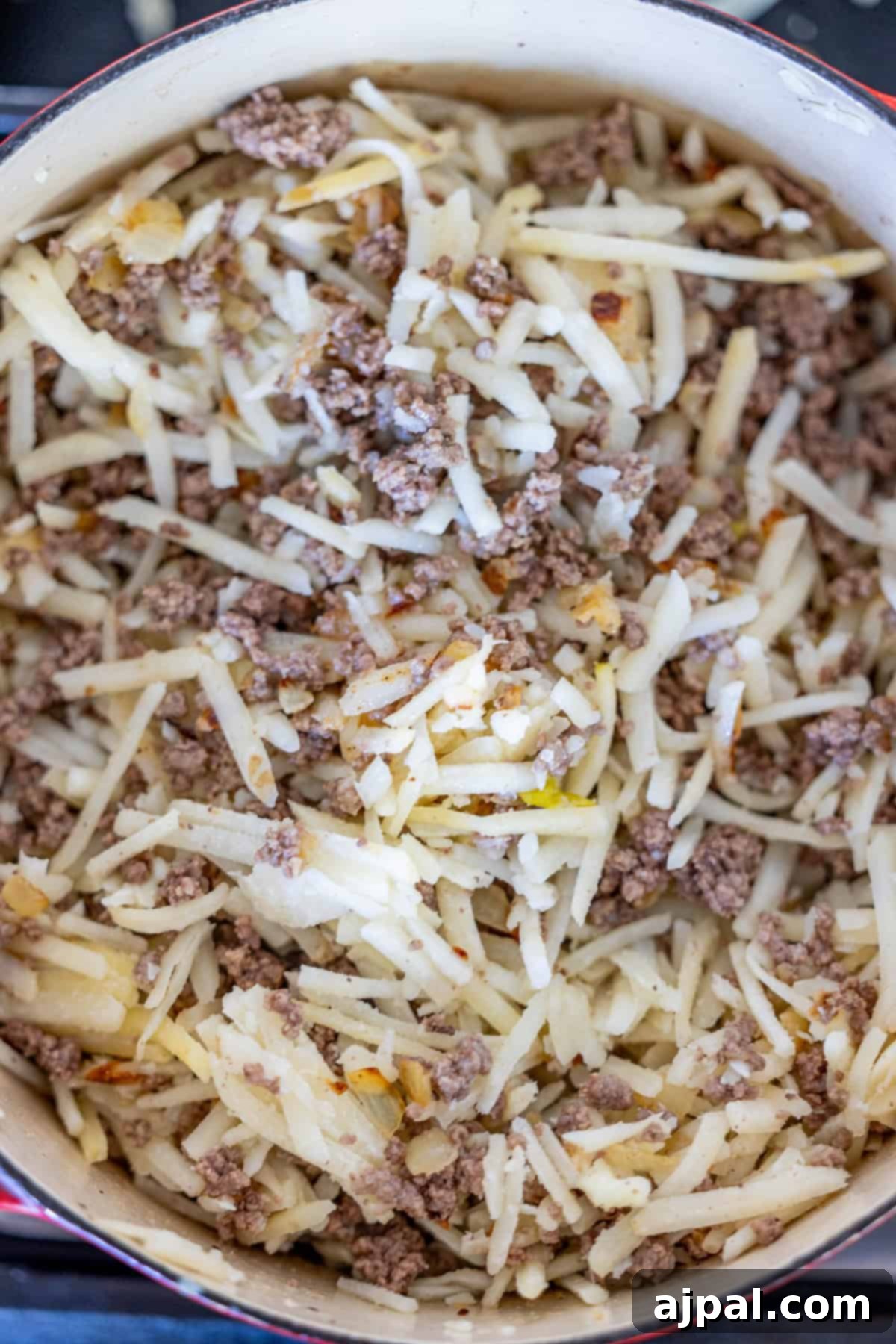 A pot filled with creamy hash brown hamburger soup, featuring cooked ground beef and shredded potatoes.