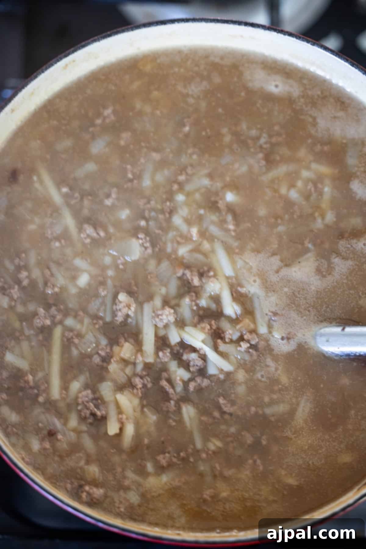 A pot of creamy hash brown hamburger soup with ground meat, onions, and noodles simmering.