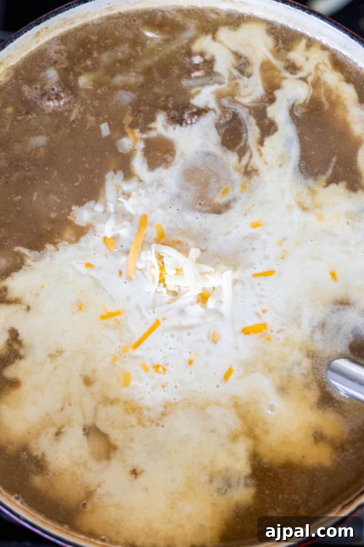 A pot of creamy hash brown soup with hamburger and cheese melting on top.