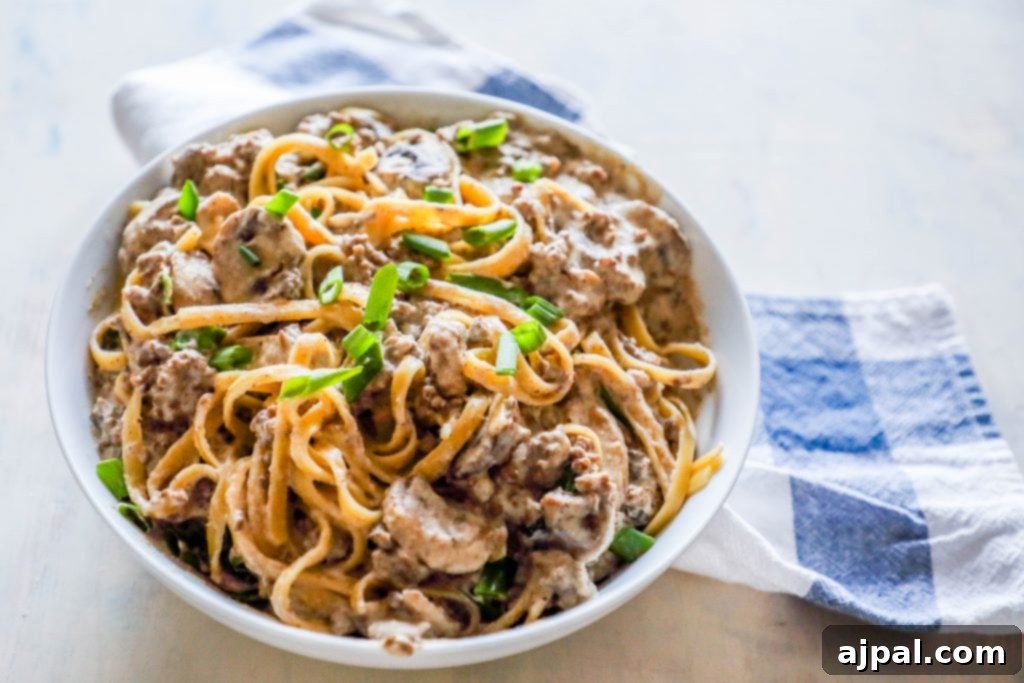 Noodles with creamy stroganoff with mushrooms and chives on top sitting on a white plate
