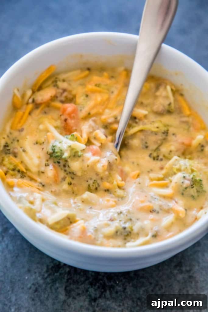 Hearty Slow Cooker Creamy Sausage and Broccoli Cheese Soup 7 A large white bowl filled with creamy sausage and broccoli cheese soup, with a serving spoon resting in it, ready to be enjoyed.