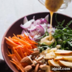 A bowl of salad with carrots, apples and a dressing being poured over it with arugula.