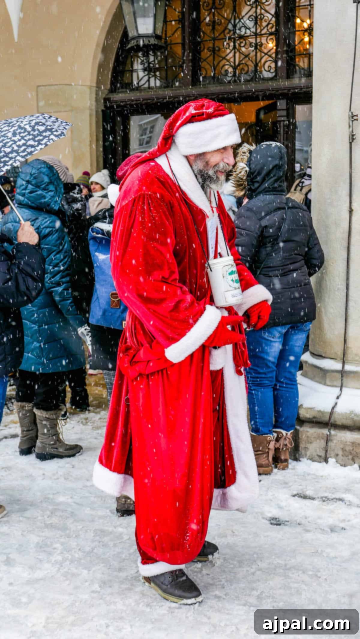 A person in a Santa costume stands outdoors in the snow, holding a donation tin. Surrounded by people, they bring festive cheer reminiscent of the Krakow Nativity Competition.