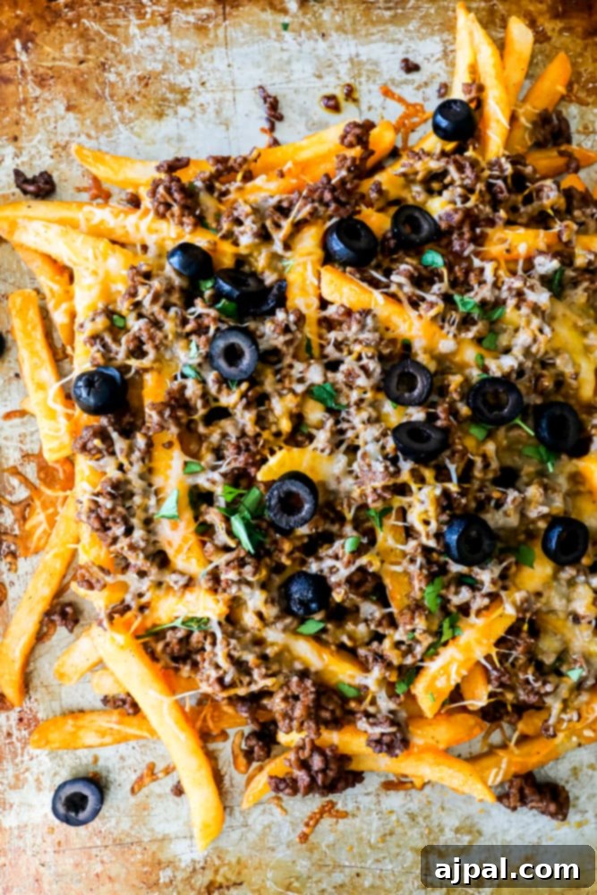 Game Day Feast: 12 Must-Try Dishes 14 A sheet pan loaded with crispy golden fries generously topped with melted cheese, seasoned ground meat, jalapeños, olives, and fresh cilantro, resembling a fusion of nachos and fries.