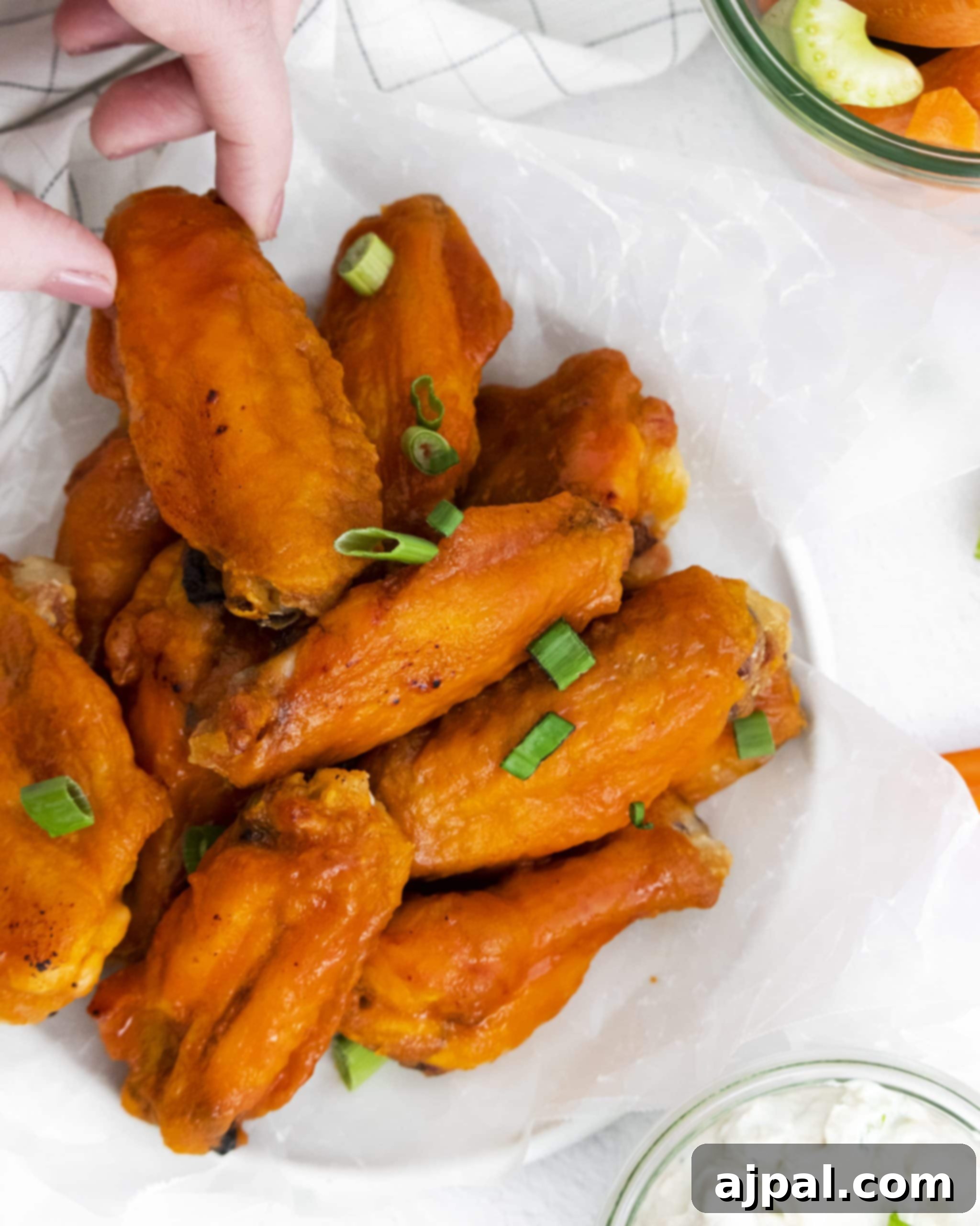 Game Day Feast: 12 Must-Try Dishes 3 Golden brown honey buffalo chicken wings drizzled with sauce on a white plate, accompanied by a small bowl of dipping sauce and fresh celery sticks.