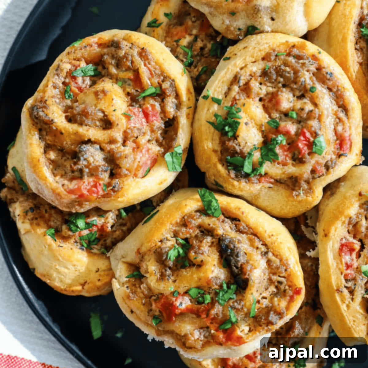 Game Day Feast: 12 Must-Try Dishes 8 A close-up of savory sausage cream cheese pinwheels arranged on a black plate, showcasing their spiraled layers of puff pastry, seasoned sausage, and creamy cheese filling.