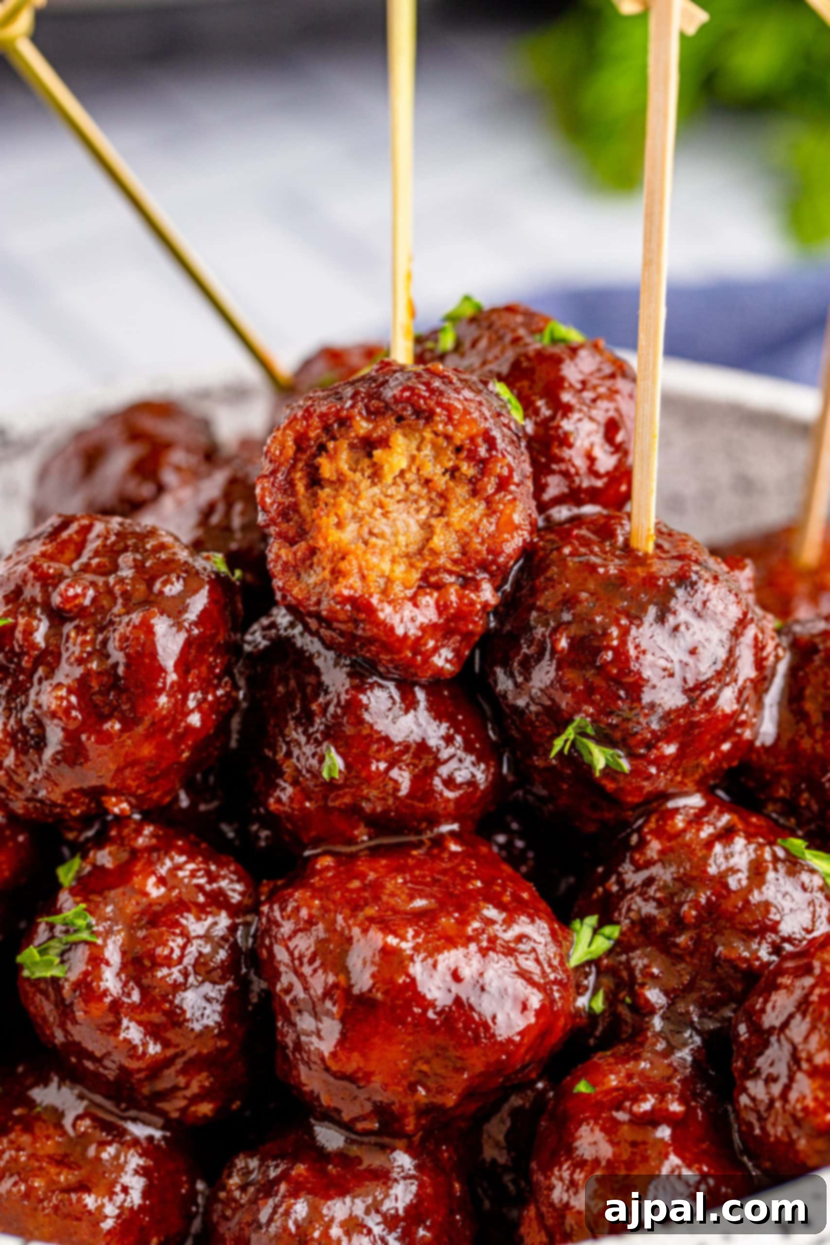 Game Day Feast: 12 Must-Try Dishes 10 A large bowl filled with glossy, dark slow cooker grape jelly meatballs, garnished with fresh parsley, ready to be served as a sweet and savory party appetizer.