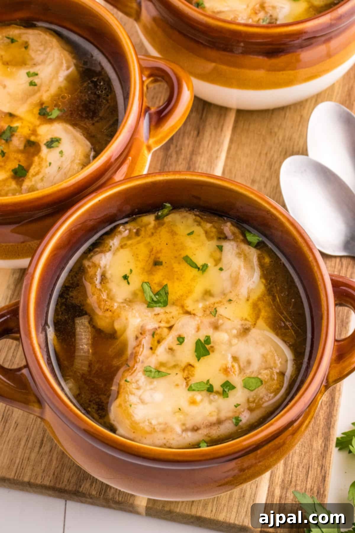 Hearty Homemade French Onion Soup 3 Three rustic bowls of French Onion Soup, garnished with fresh parsley, sitting on a wooden cutting board, ready to be served.