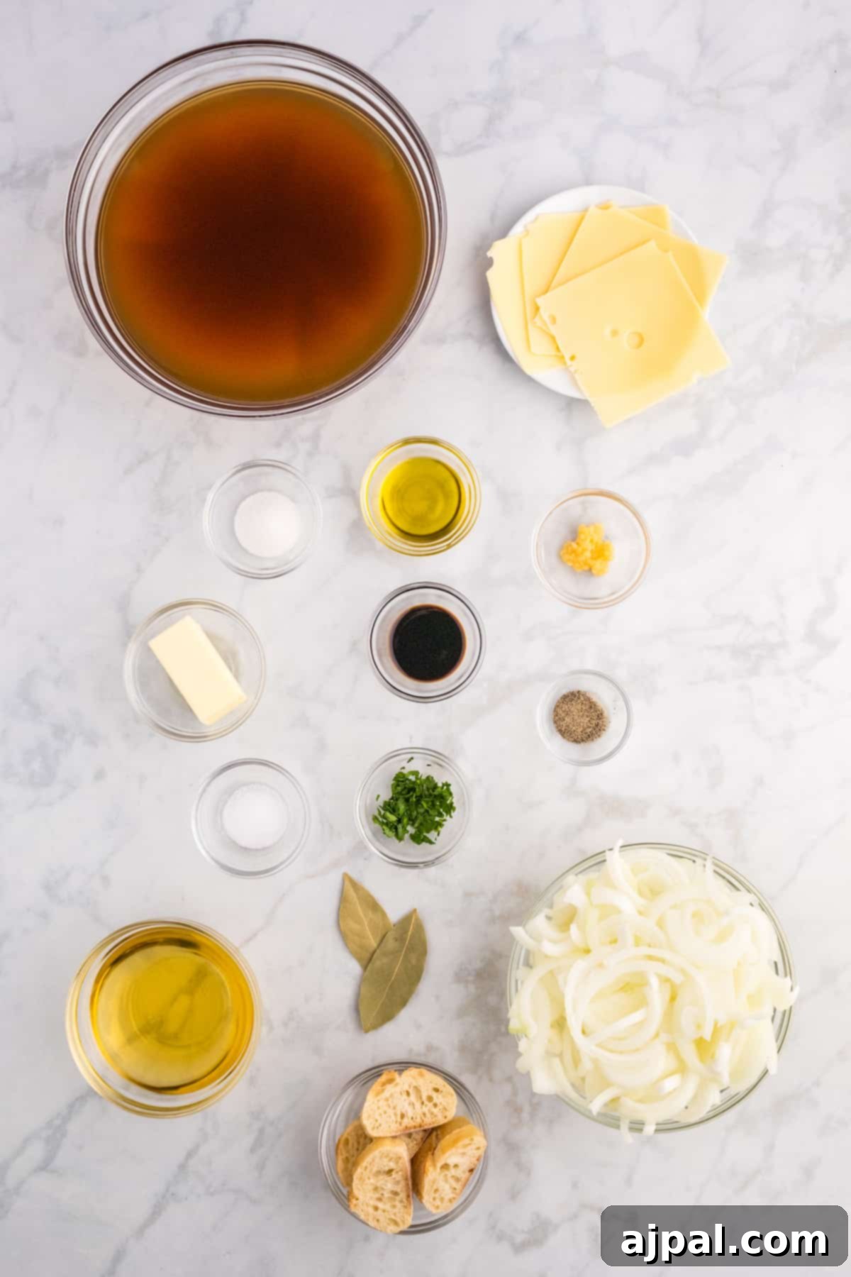 Hearty Homemade French Onion Soup 5 A collection of fresh ingredients for French Onion Soup, including large yellow onions, a block of Gruyère cheese, a bottle of red wine, and various herbs and spices, artfully arranged on a marble countertop.