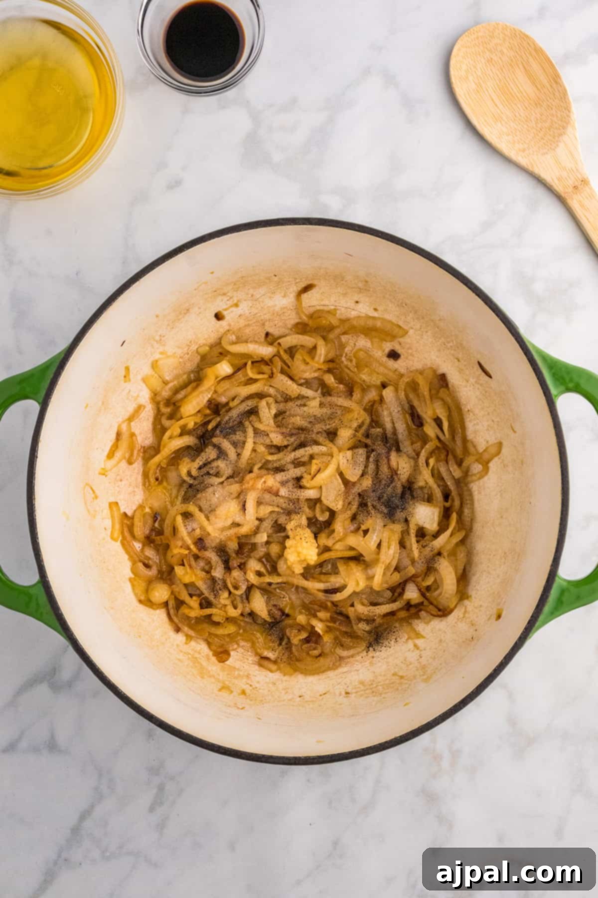 Golden-brown caramelized onions simmering in a pan, being gently stirred with a wooden spoon, the essence of French Onion Soup.