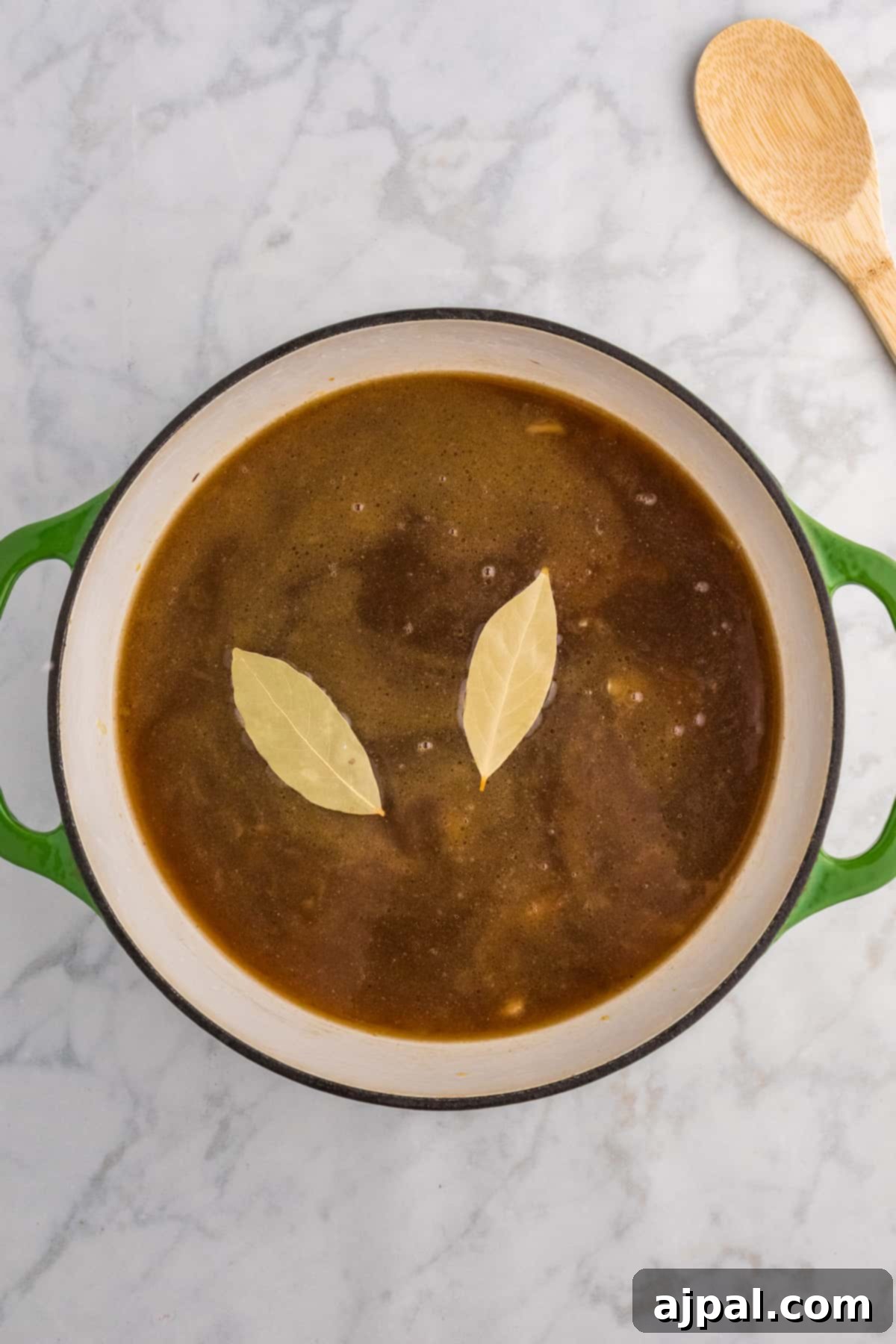 Fresh sage leaves and a wooden spoon resting beside a pan of reducing French Onion Soup, enhancing its aromatic depth.