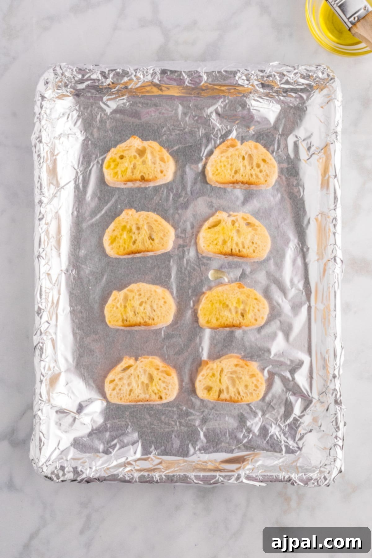 A baking sheet filled with golden-brown breadsticks, lightly oiled and ready to be used as croutons for French Onion Soup.