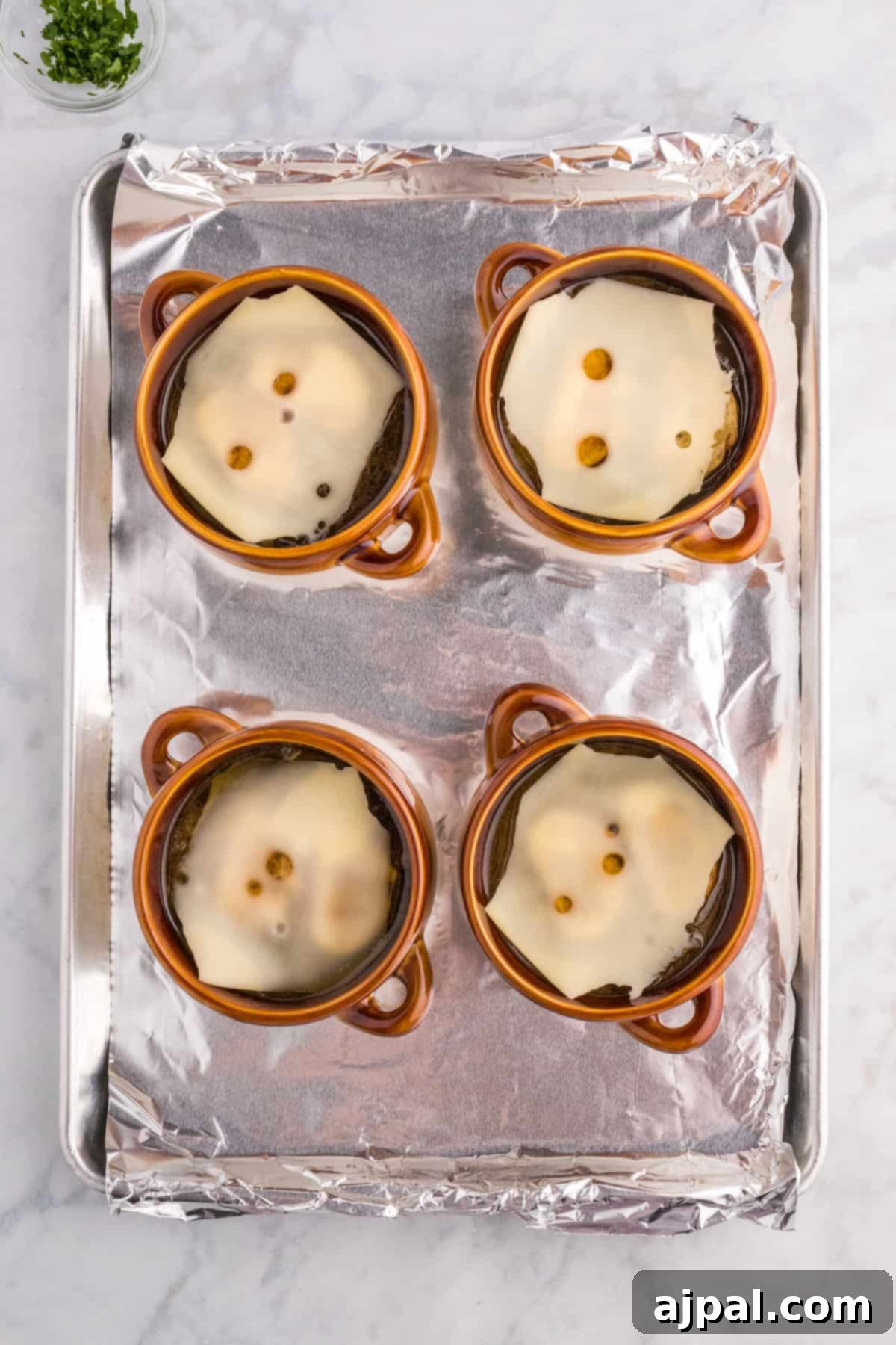 Four individual oven-safe bowls filled with French Onion Soup base, topped with bread slices, ready for a generous layer of Gruyère cheese and broiling.