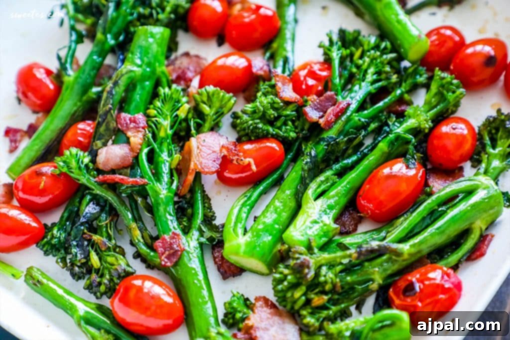 Close-up of charred broccolini, crispy bacon, and glistening cherry tomatoes on a white plate, highlighting the textures.
