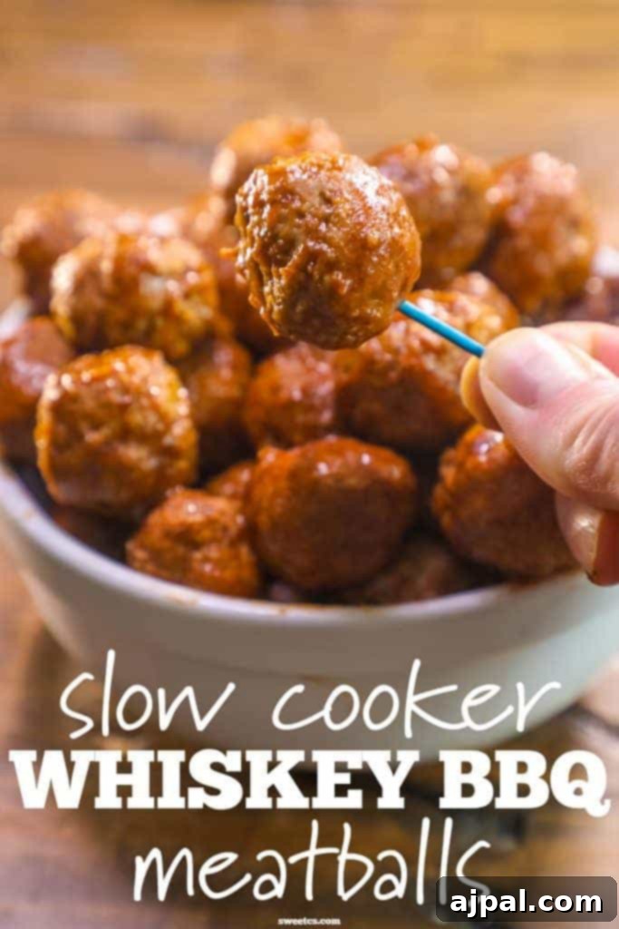 A close-up shot of a single whiskey BBQ meatball perfectly skewered on a toothpick, with a blurred bowl of more delicious meatballs in the background, ready for a party.