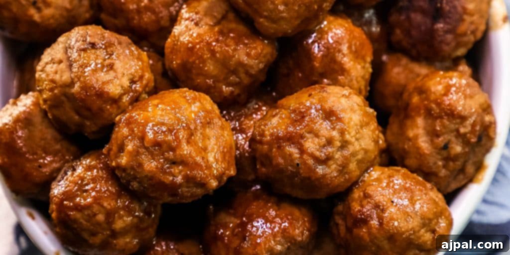 A close-up view of succulent whiskey BBQ meatballs, glistening with a rich, dark sauce in a white serving bowl, ready to be enjoyed.