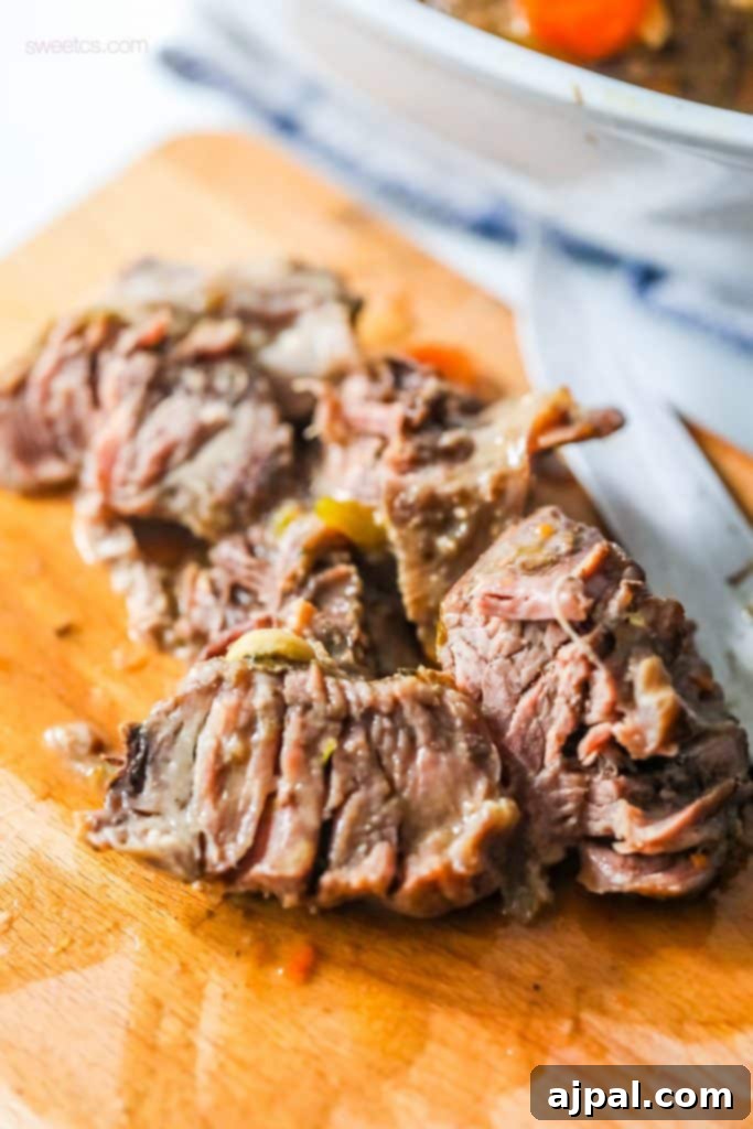 Tender pot roast beef on a wooden cutting board with a silver carving knife.