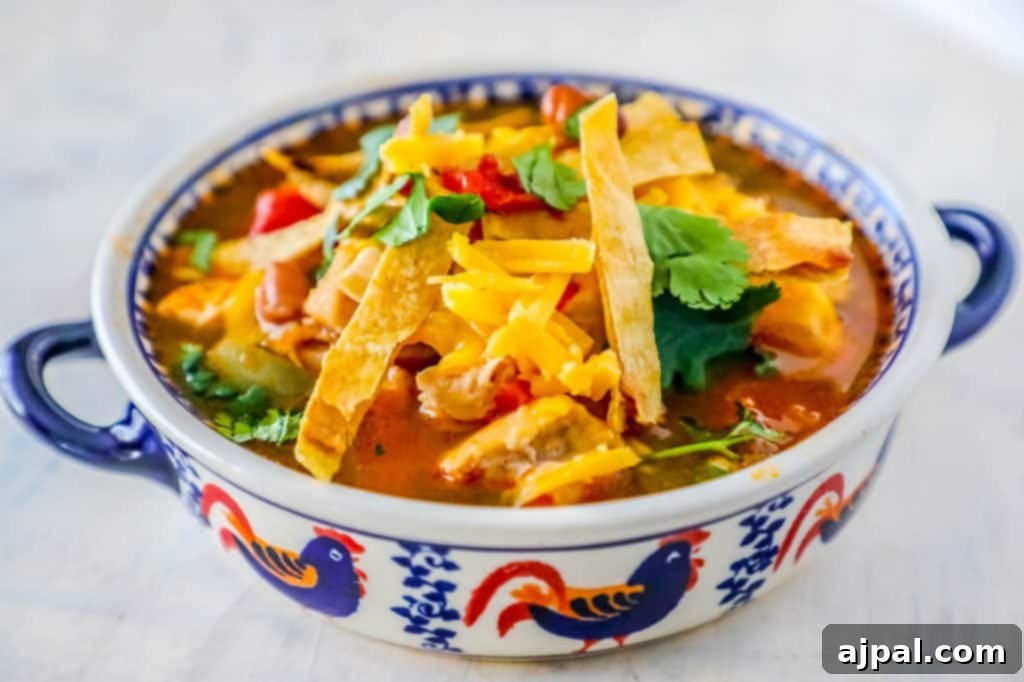 A vibrant bowl of Mexican chicken tortilla soup, generously topped with cilantro, shredded cheese, and crispy tortilla strips, ready to be enjoyed.
