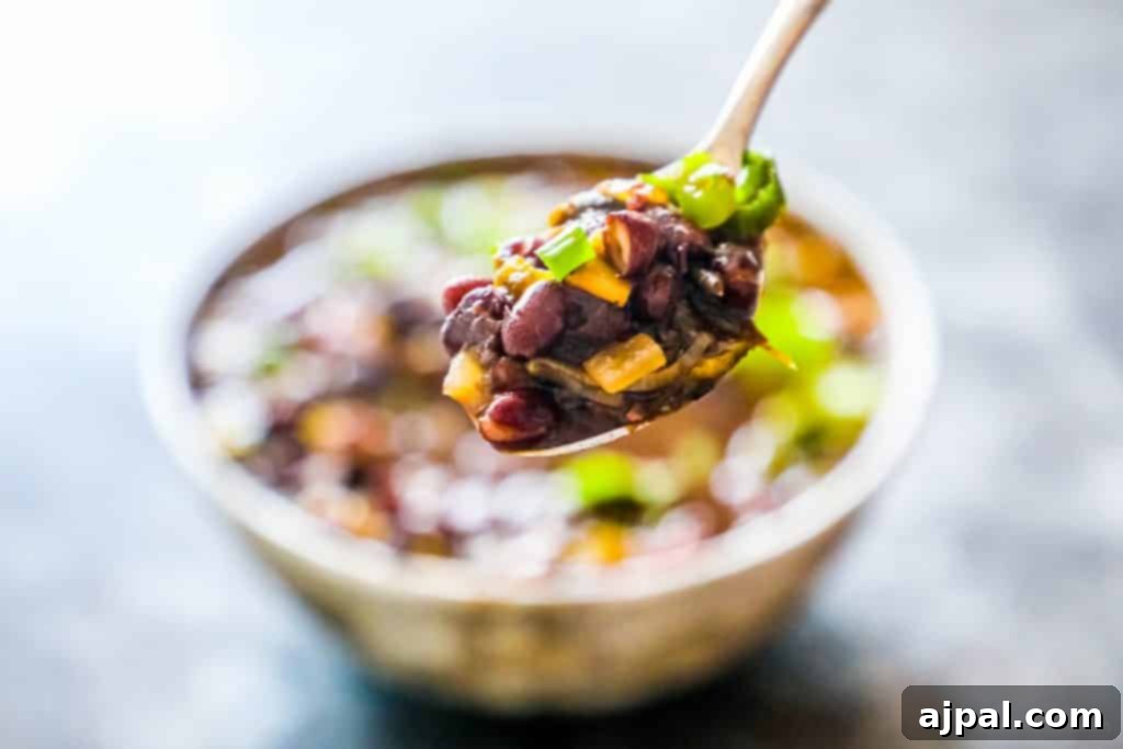 A serving spoon lifting a generous portion of spicy black bean soup, topped with green onions, from a bowl.