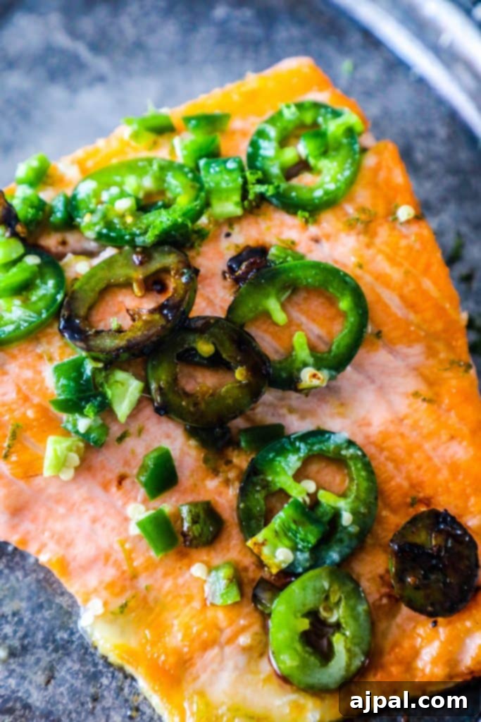 Honey Lime Glazed Jalapeno Salmon 2 Perfectly cooked salmon fillets adorned with vibrant green jalapeno slices and a glossy honey-lime glaze, resting on a metal baking sheet.