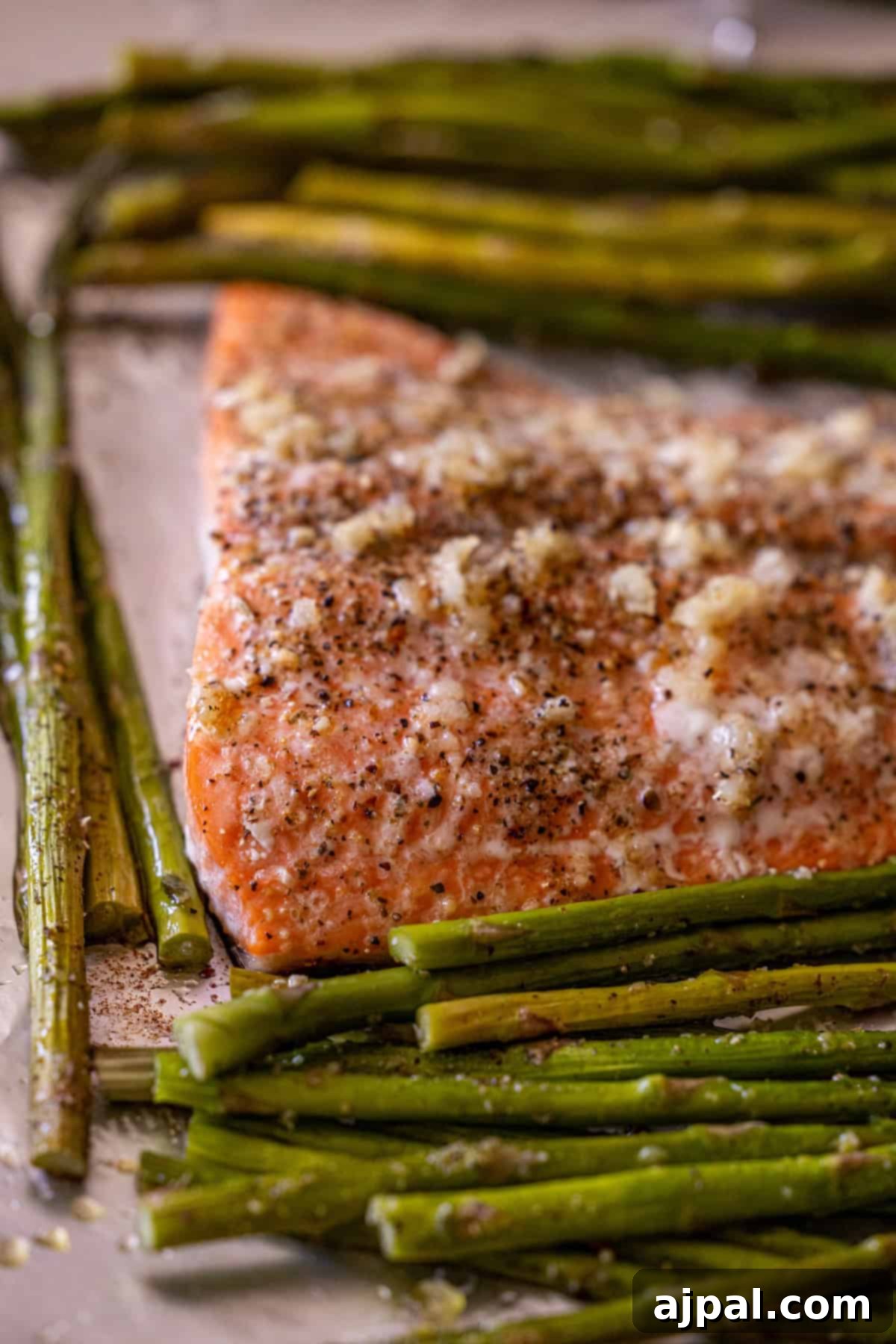Zesty Sheet Pan Lemon Garlic Salmon and Asparagus 9 A baked salmon fillet seasoned with pepper and garlic is surrounded by cooked asparagus spears on a baking sheet—an easy salmon and asparagus recipe perfect for weeknight dinners.