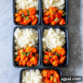 Four black plastic containers with sweet and sour chicken and rice in them.