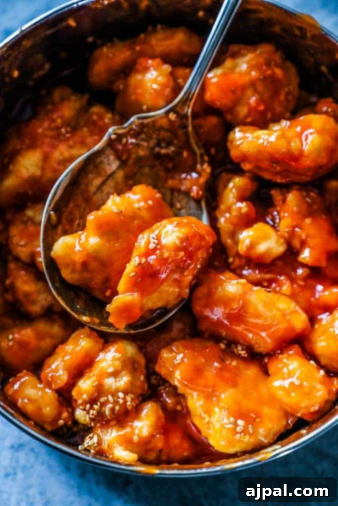 A close-up of Instant Pot Sweet and Sour Chicken in a bowl, garnished with sesame seeds and chives, with a spoon taking a scoop.