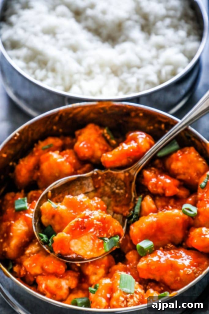 A bowl of Instant Pot Sweet and Sour Chicken and Rice with a spoon, highlighting the rich orange sauce and perfectly cooked rice.