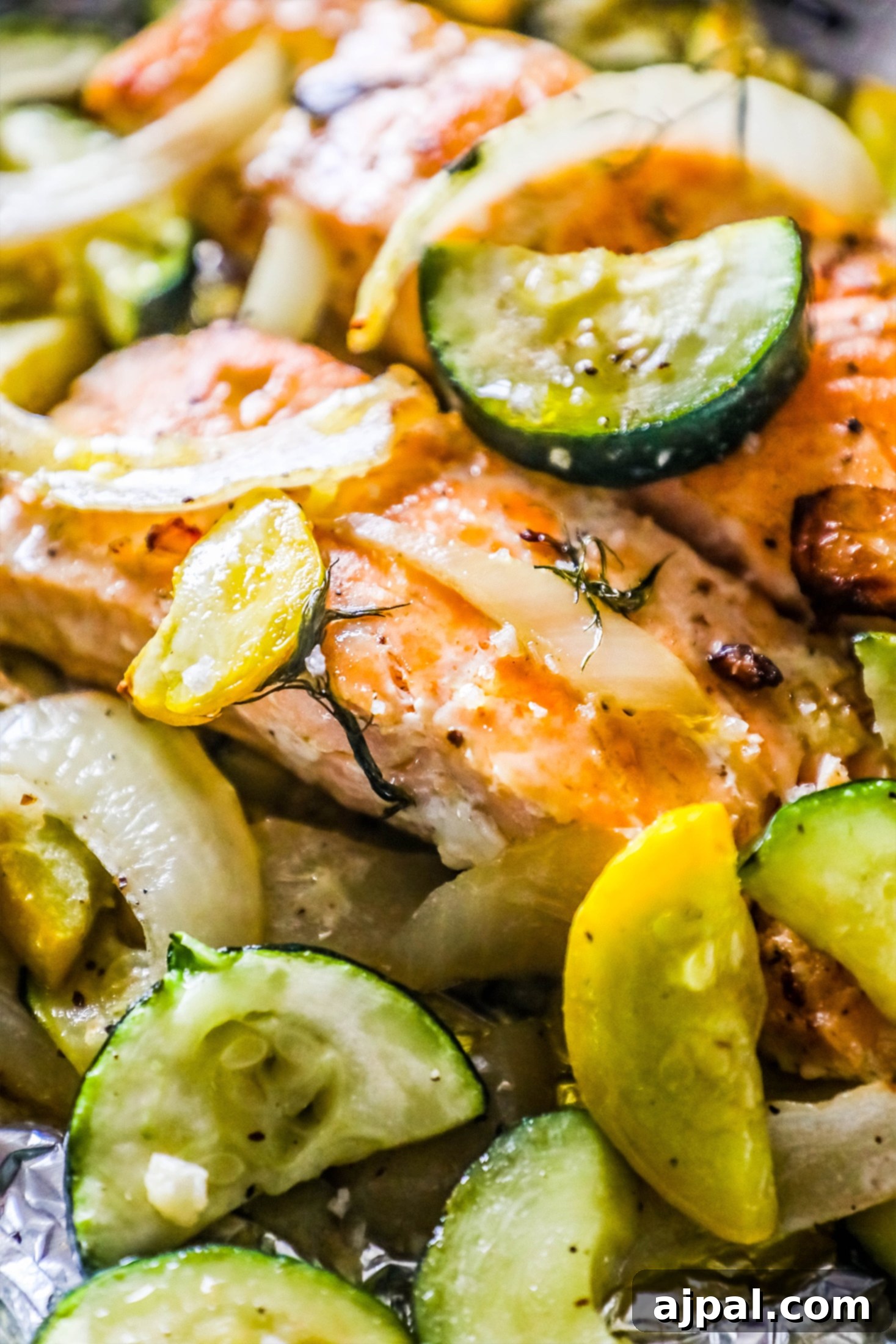Garlic Herb Salmon and Zucchini Foil Packs 2 Succulent salmon fillets adorned with fresh dill and garlic, nestled among vibrant zucchini, yellow squash, and red onion slices, ready to be cooked in a foil packet.