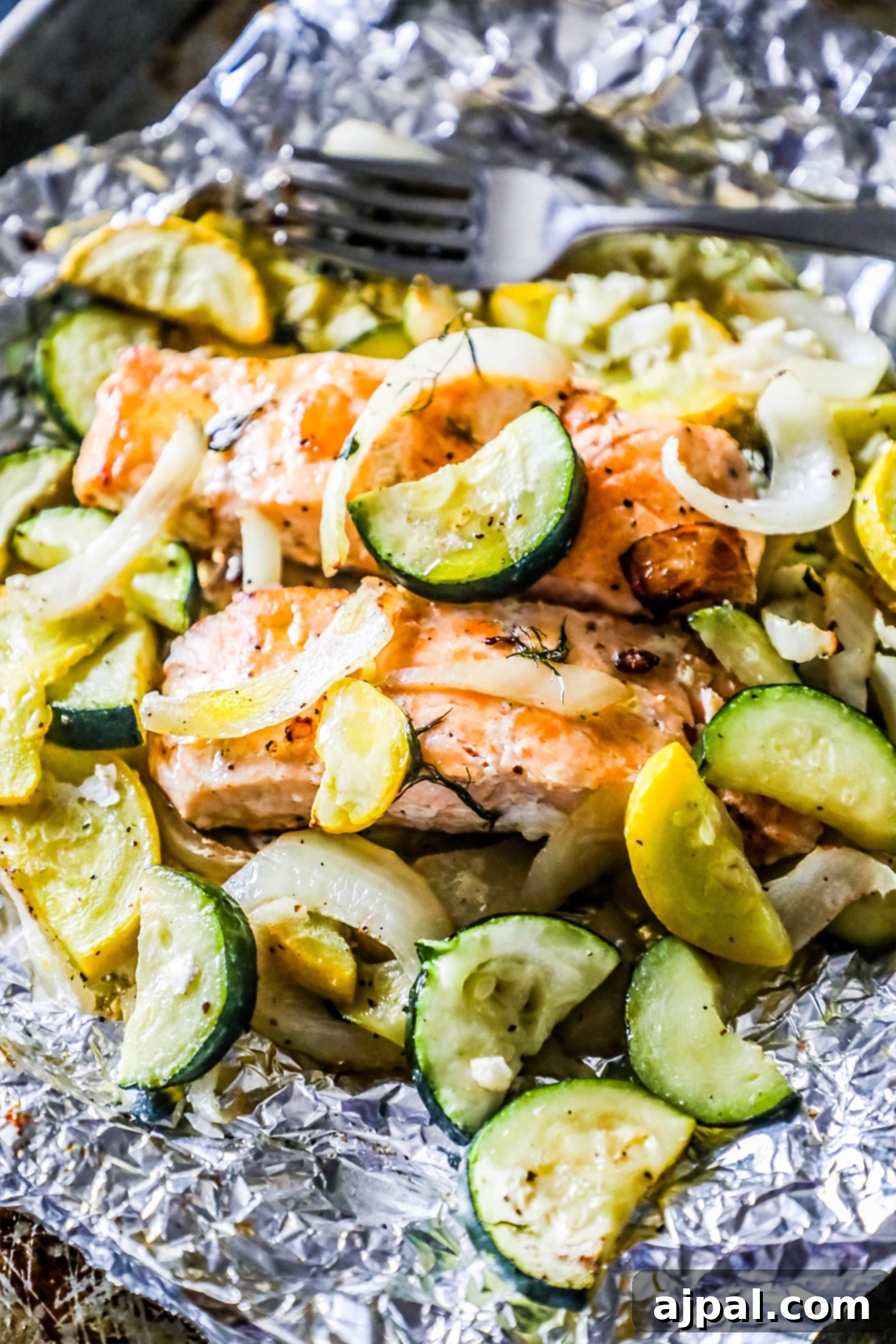 Garlic Herb Salmon and Zucchini Foil Packs 3 A garlic herb salmon fillet with dill, surrounded by zucchini, squash, and onion, perfectly cooked inside an open foil pouch, steam gently rising.
