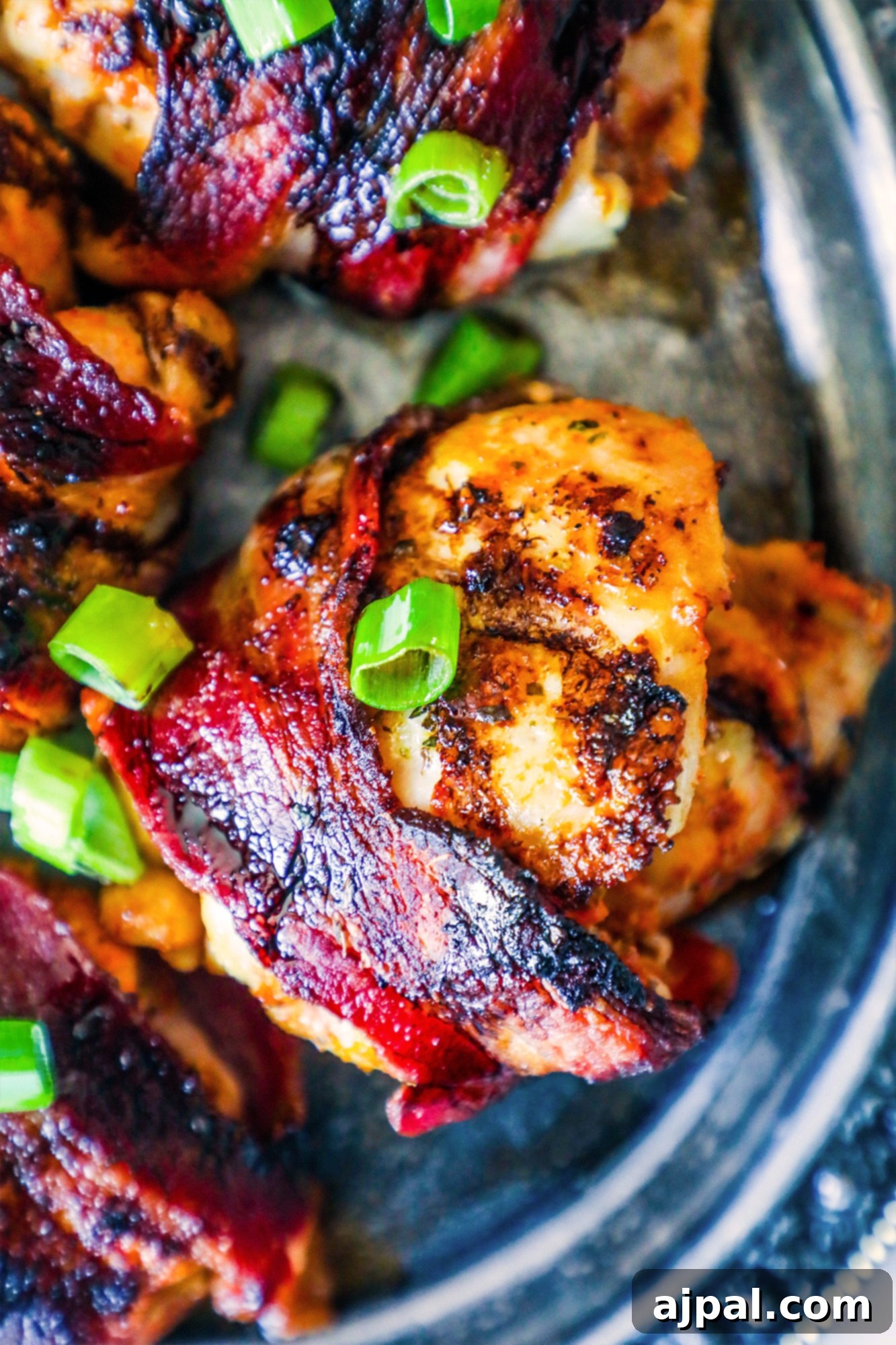 Sweet and Smoky Balsamic Bacon Chicken Thighs 2 Succulent bacon-wrapped chicken thighs, glistening with balsamic glaze and garnished with fresh green onions, presented beautifully on a silver platter.