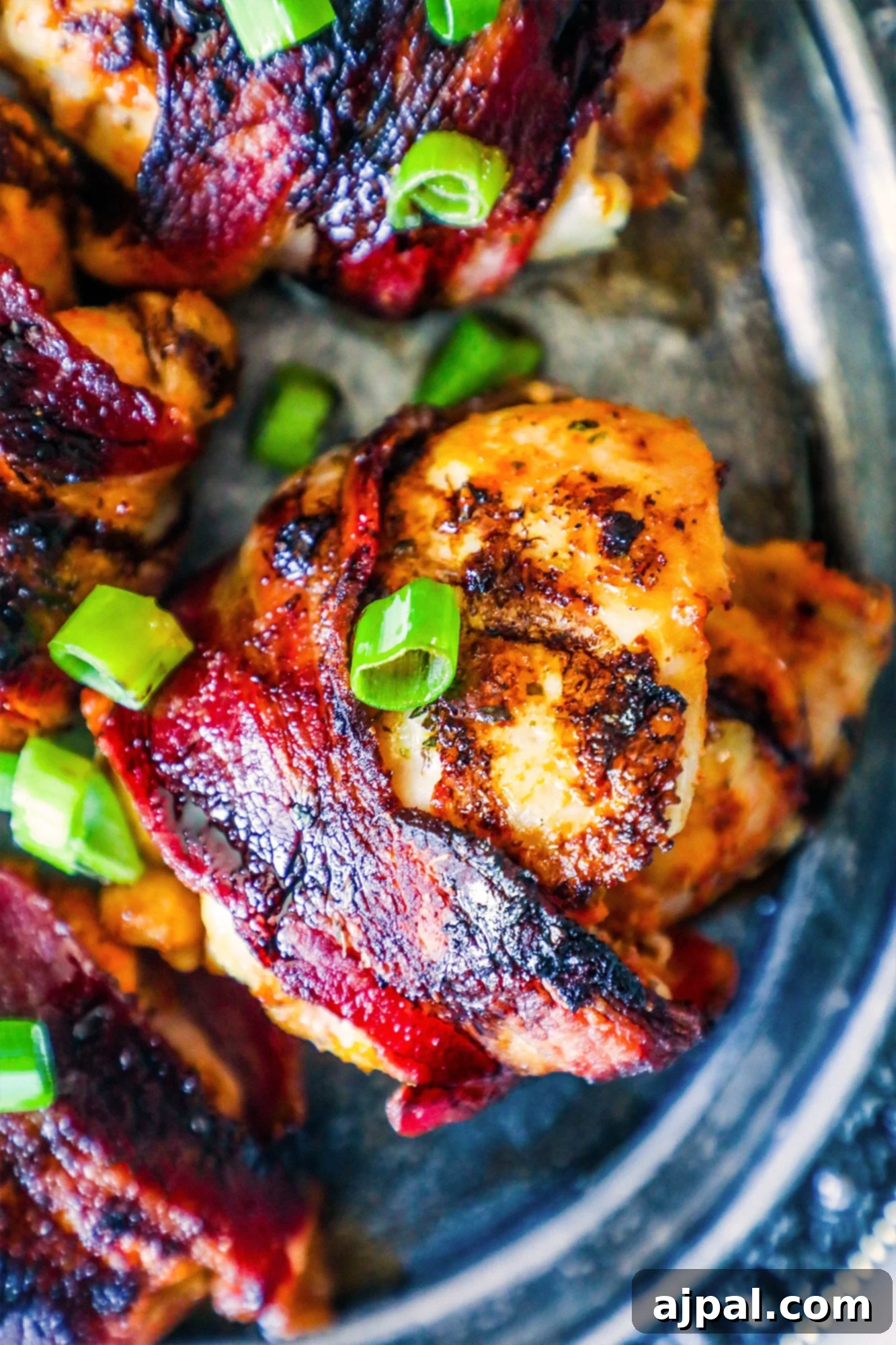 Sweet and Savory Balsamic Bacon Chicken Thighs 2 Close-up shot of perfectly cooked bacon-wrapped chicken thighs on a silver plate, garnished with fresh green onions.