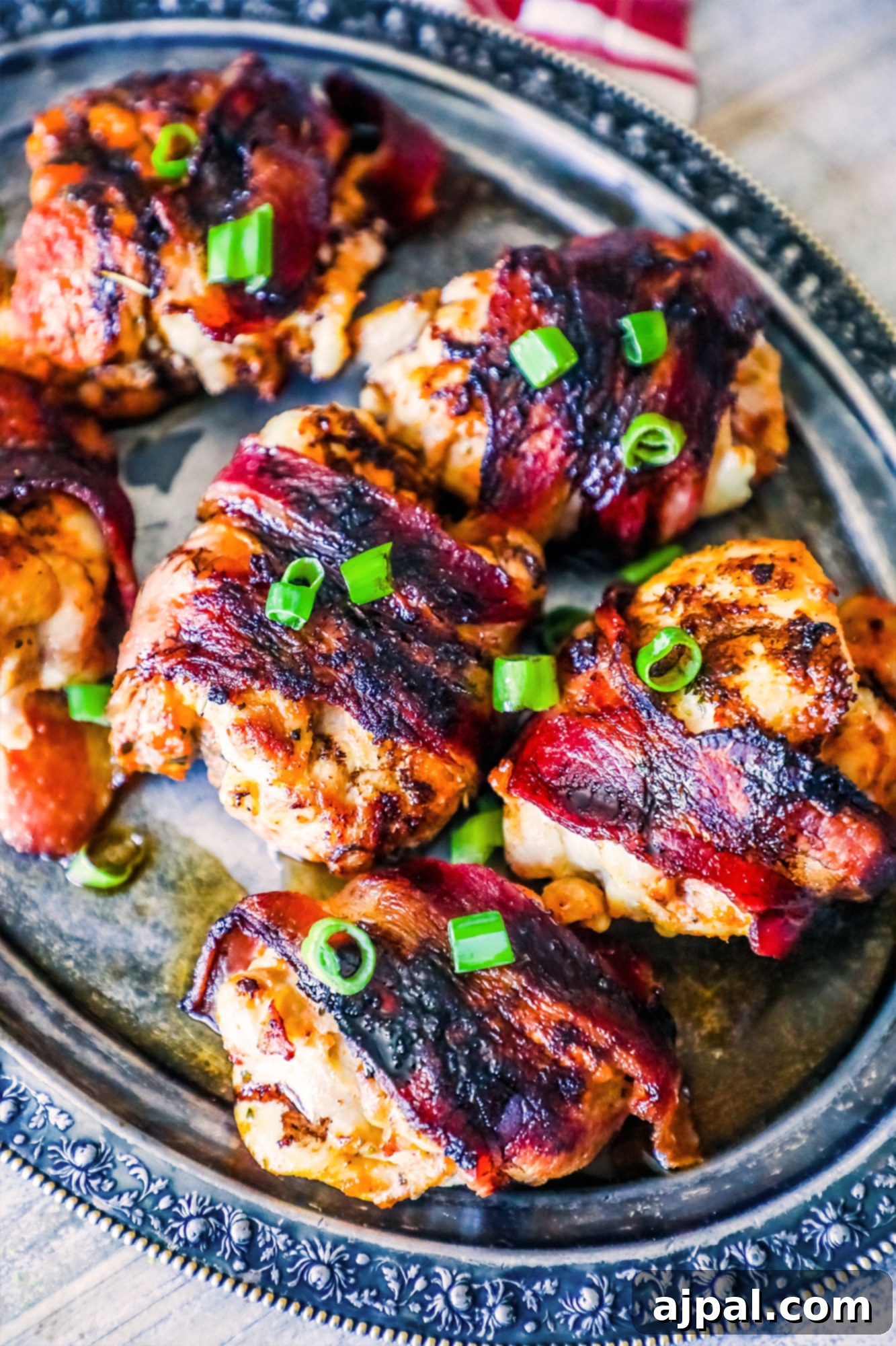 Sweet and Smoky Balsamic Bacon Chicken Thighs 3 Perfectly cooked bacon-wrapped chicken thighs, glazed with balsamic vinegar, and sprinkled with fresh green onions, resting on a elegant silver plate.