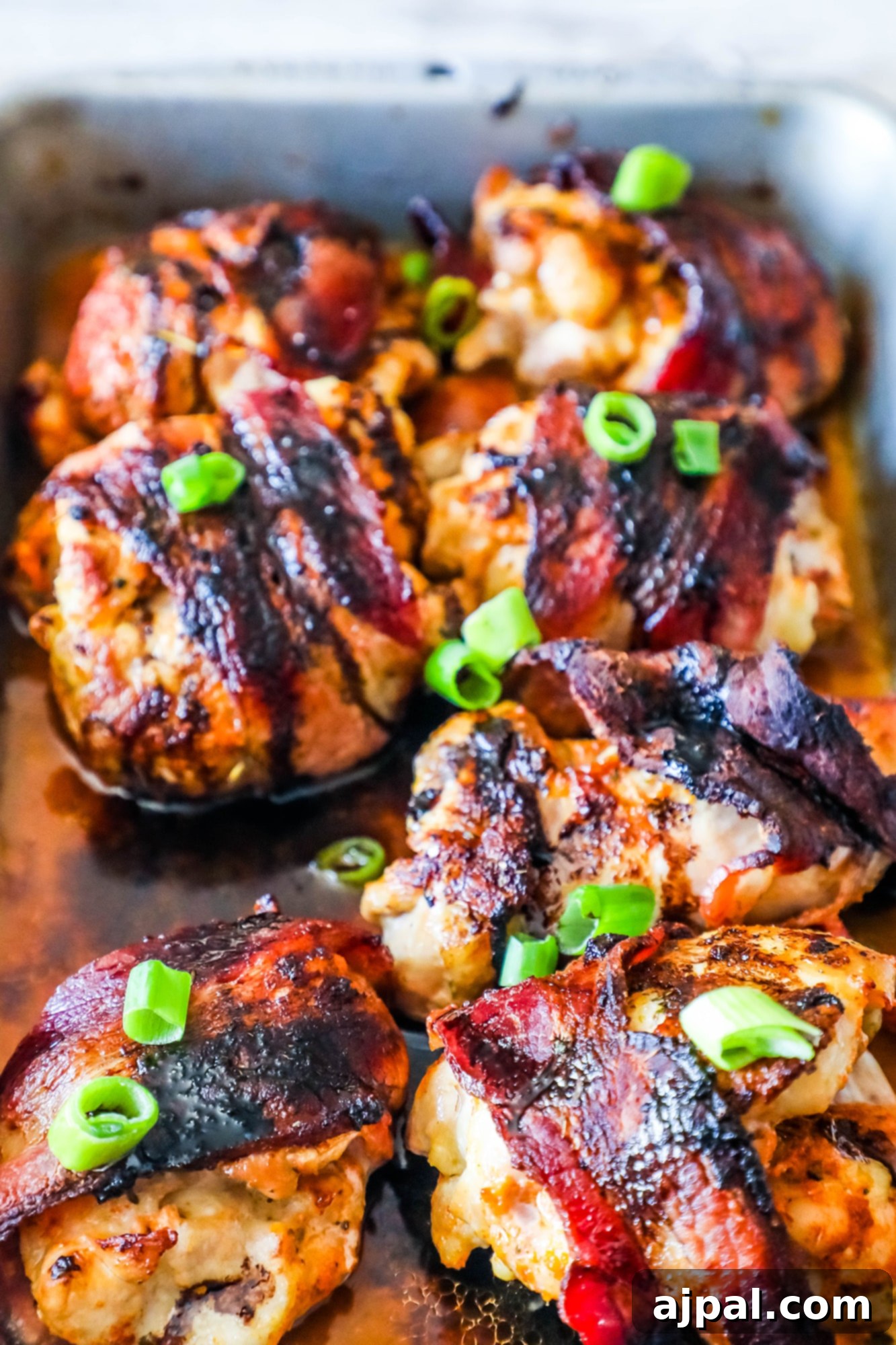 Sweet and Smoky Balsamic Bacon Chicken Thighs 4 A close-up of a perfectly grilled balsamic glazed chicken thigh, wrapped in crispy bacon and topped with vibrant green onions, ready to be enjoyed.