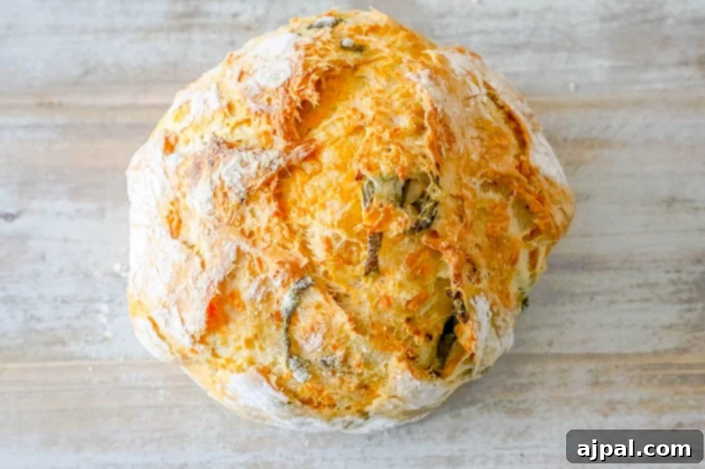 A rustic, round loaf of homemade Jalapeño Cheddar Dutch Oven Bread on a wooden table.