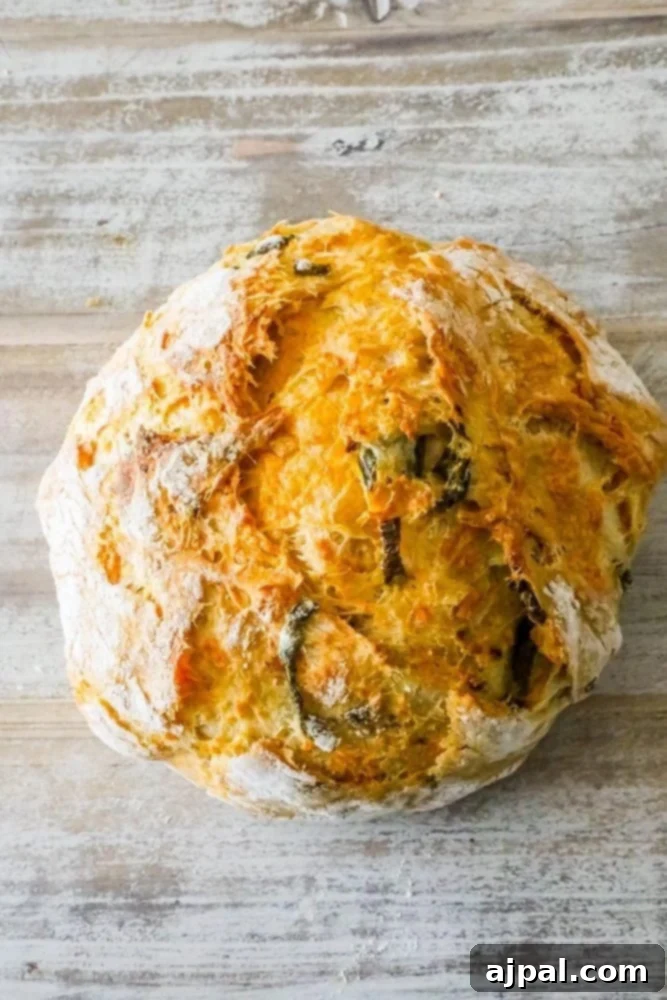 Round loaf of jalapeño cheddar bread with baked-in cheese and peppers on a wooden table