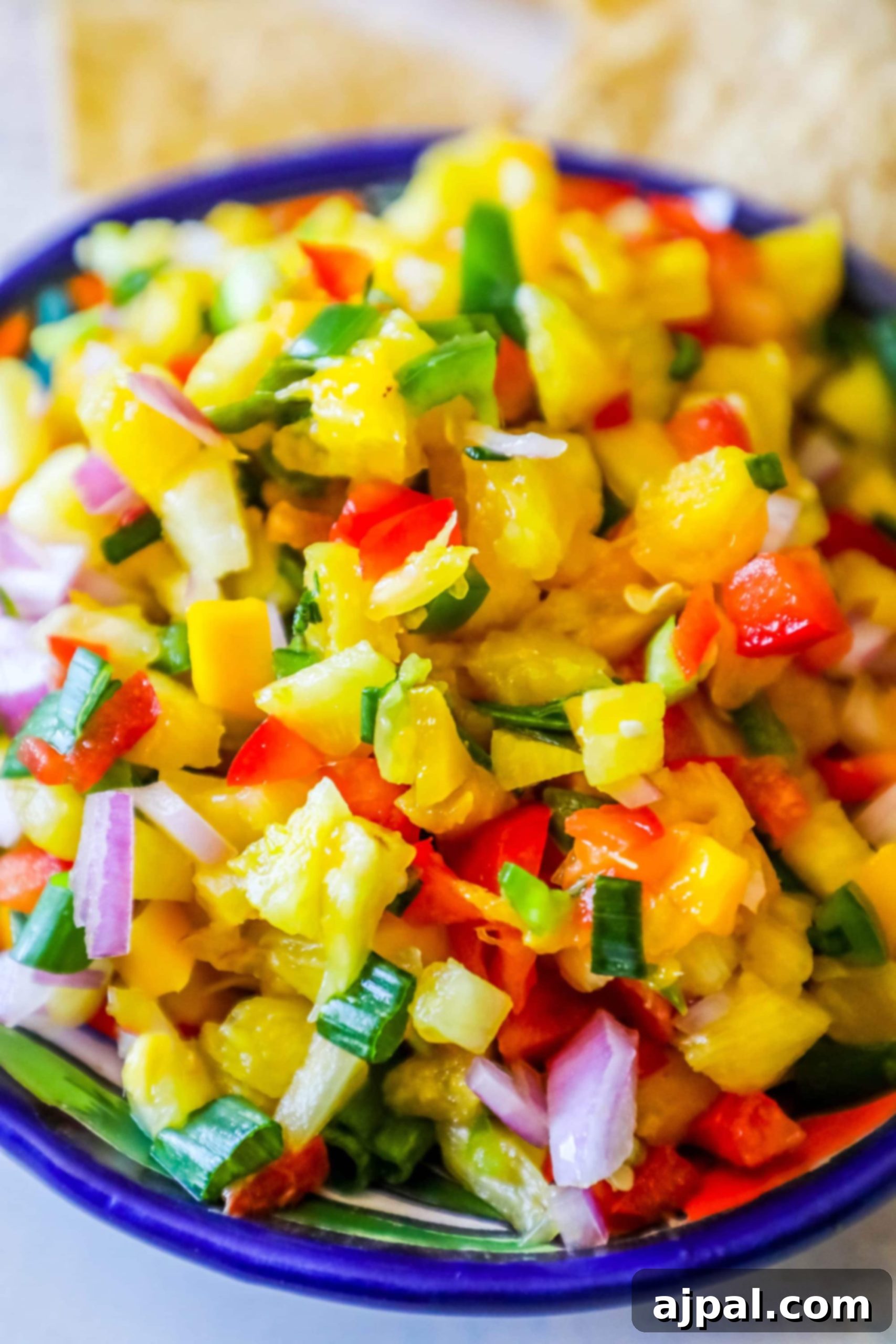 bowl with pineapple, jalapeno, red onion, and green onions, chips behind it
