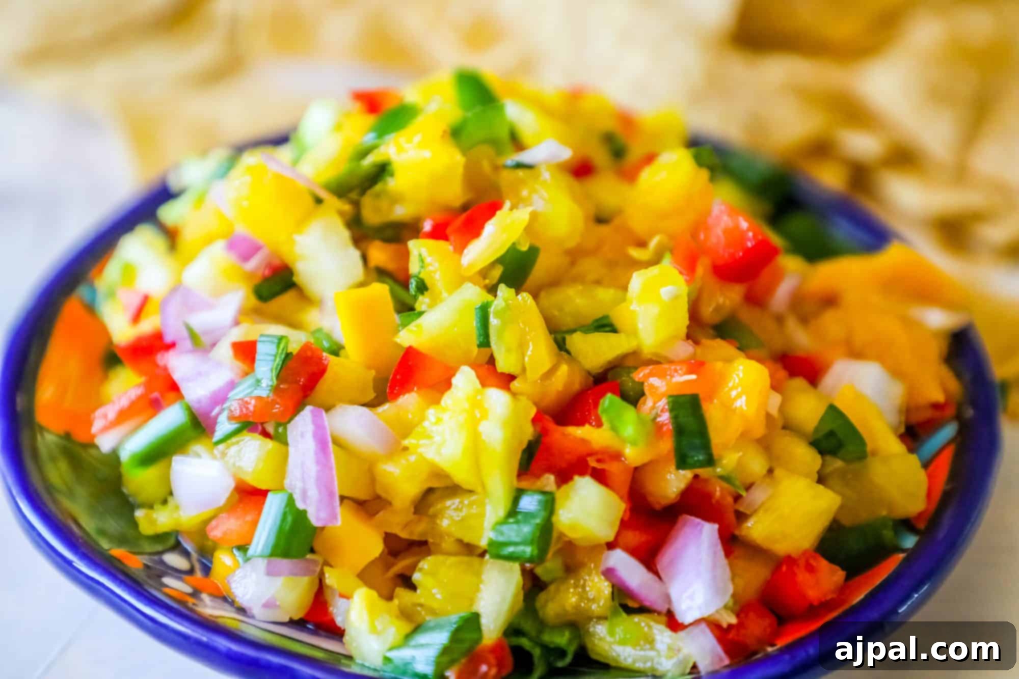 bowl with pineapple, jalapeno, red onion, and green onions, chips behind it
