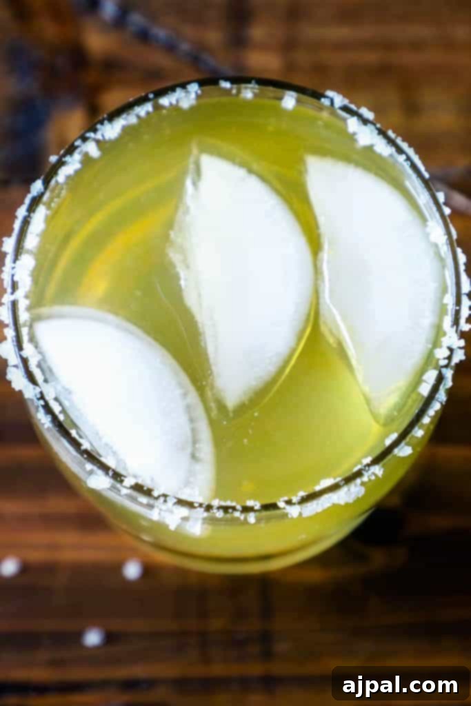 A vibrant Beer-ita cocktail in a salt-rimmed glass, garnished with lime, on a wooden table.